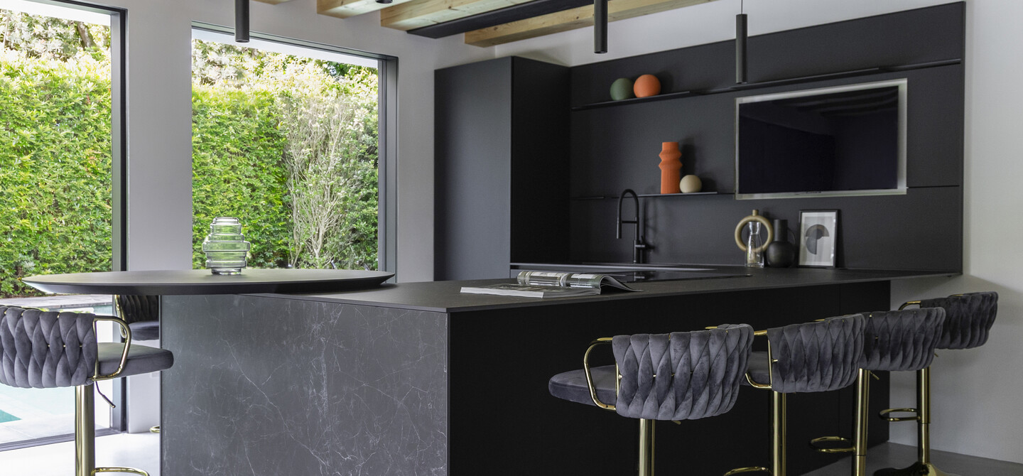 Cucina total black con penisola ampia, corredata da quattro sgabelli e un piano snack rotondo