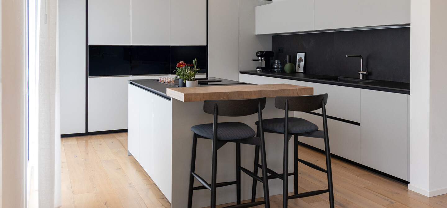 Cucina a isola in laccato bianco e dettagli bruniti aperta sul living. L’isola con piano snack divide dal resto dell’open space