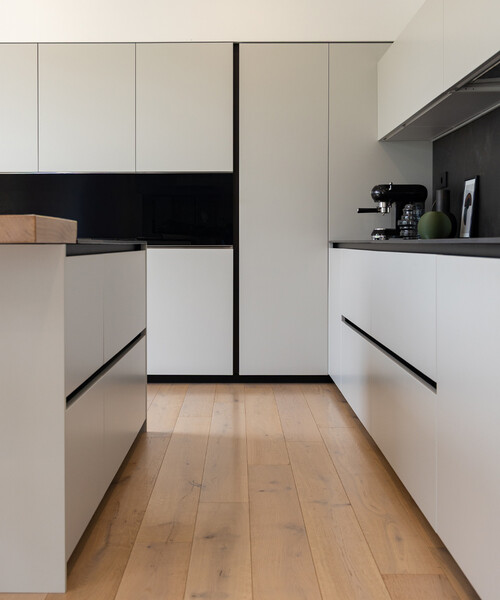 In una cucina bianca e nera, dallo stile uniforme, un dettaglio semplice come lo spesso piano snack a sbalzo in legno attrae gli sguardi.