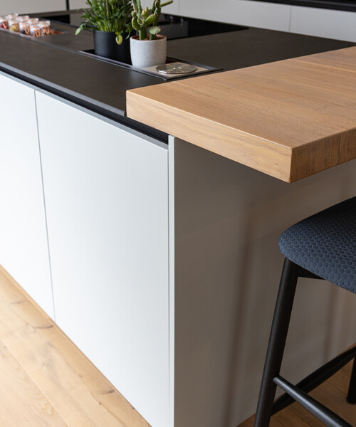 Il piano operativo sottile e scuro in Laminam Ossido nero si contrappone al piano snack spesso 6 cm in impiallacciato travi rovere safari.