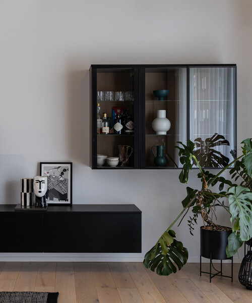 Living con mobili neri e lineari sospesi: mobile porta TV e vetrinetta. Parquet in legno e tante piante verdi.