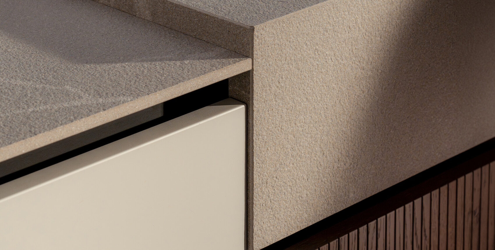 Contrasto di materiali fra basi in un liscio laccato opaco piuma e i piani di lavoro in un materico Laminam Pietra Piasentina Grigio Fiammata